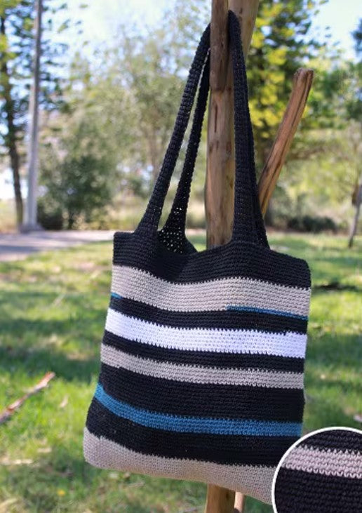 Black, white, and blue striped tote macrame bag hanging on a wooden post outdoors.